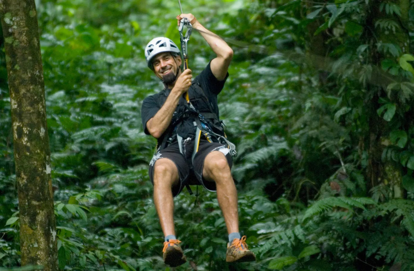 a man ziplines through a tropical rainforest and smiles, insured with travel insurance for Costa Rica 