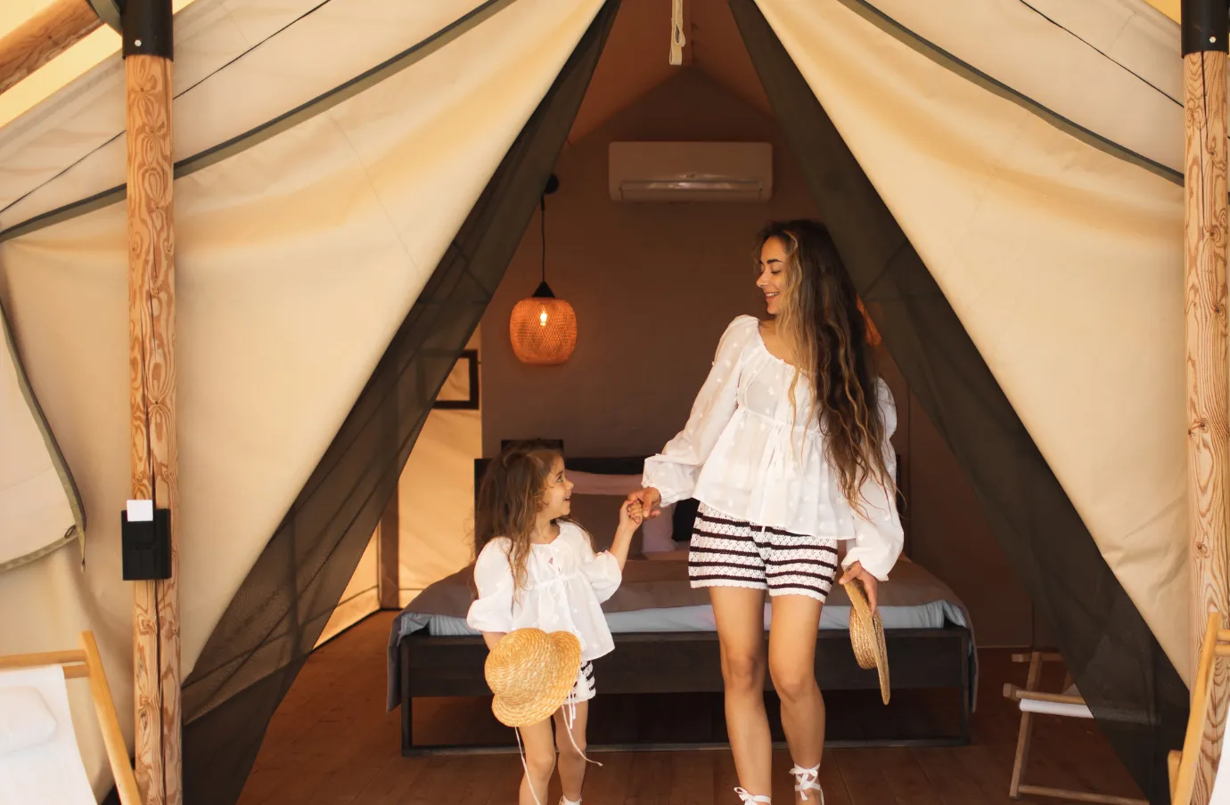 a mother and daughter hold hands as they walk out of their luxury safari tent, insured with travel insurance for Africa 