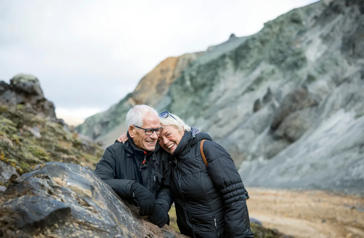 a senior couple stops for a picture while hiking lava fields, insured with travel insurance for Iceland 