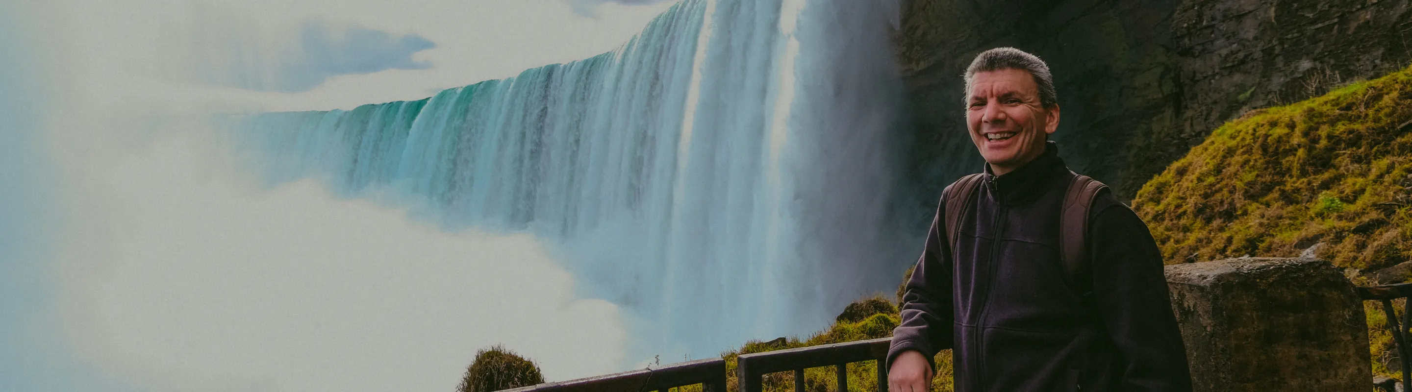 a male tourist smiles on a lookout point at Niagara Falls, insured with travel insurance for Canada