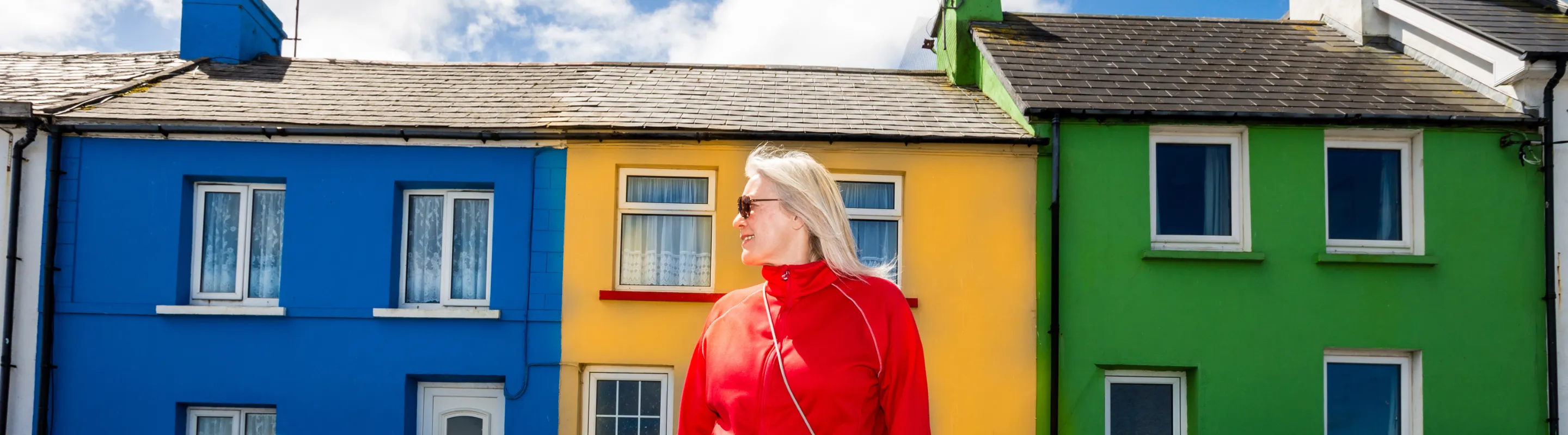 an older woman stands in an Irish street near colorful houses, insured with travel insurance for Ireland 