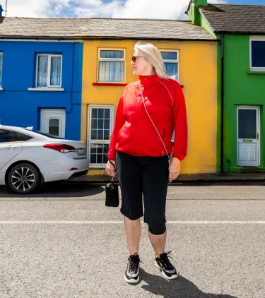 an older woman stands in an Irish street near colorful houses, insured with travel insurance for Ireland 