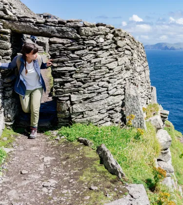 a young adult female hikes through the Skellig Michael ruins by the ocean, insured with travel insurance for Ireland