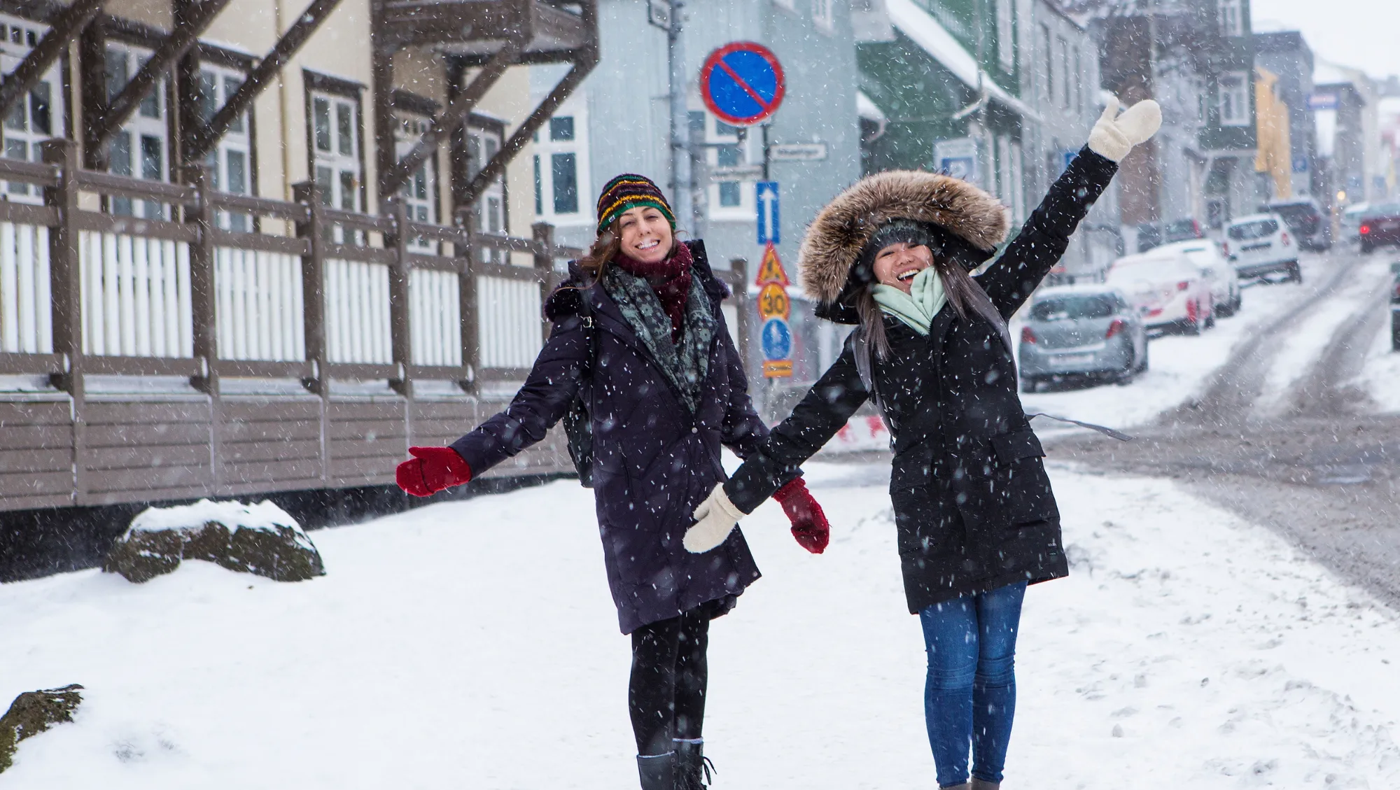 two women enjoy snowfall in the town of Reykjavik after researching, "Does travel insurance cover snowstorms?"