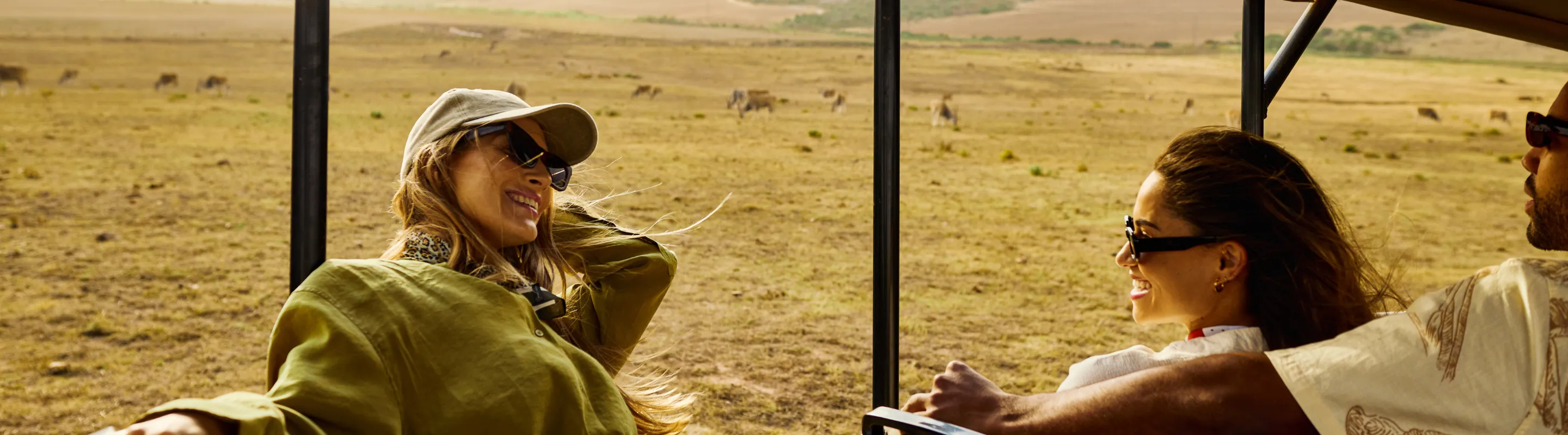 traveling young adult friends sit on an open-air safari vehicle, insured with travel insurance for Africa 