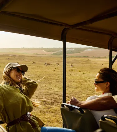 traveling young adult friends sit on an open-air safari vehicle, insured with travel insurance for Africa 