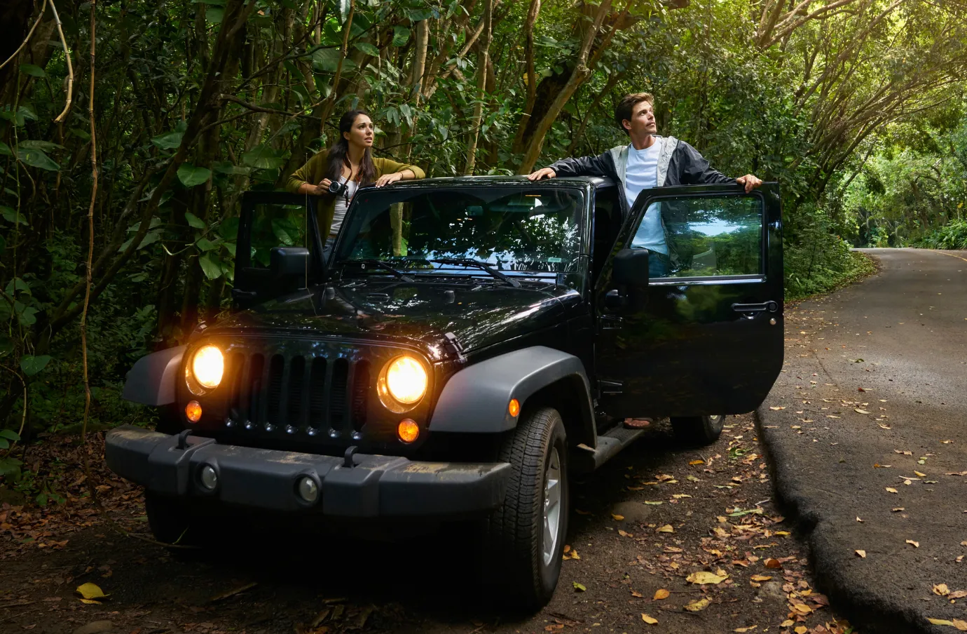 two travelers exit their jeep along a rainforest road, hoping to avoid a vehicle accident on vacation