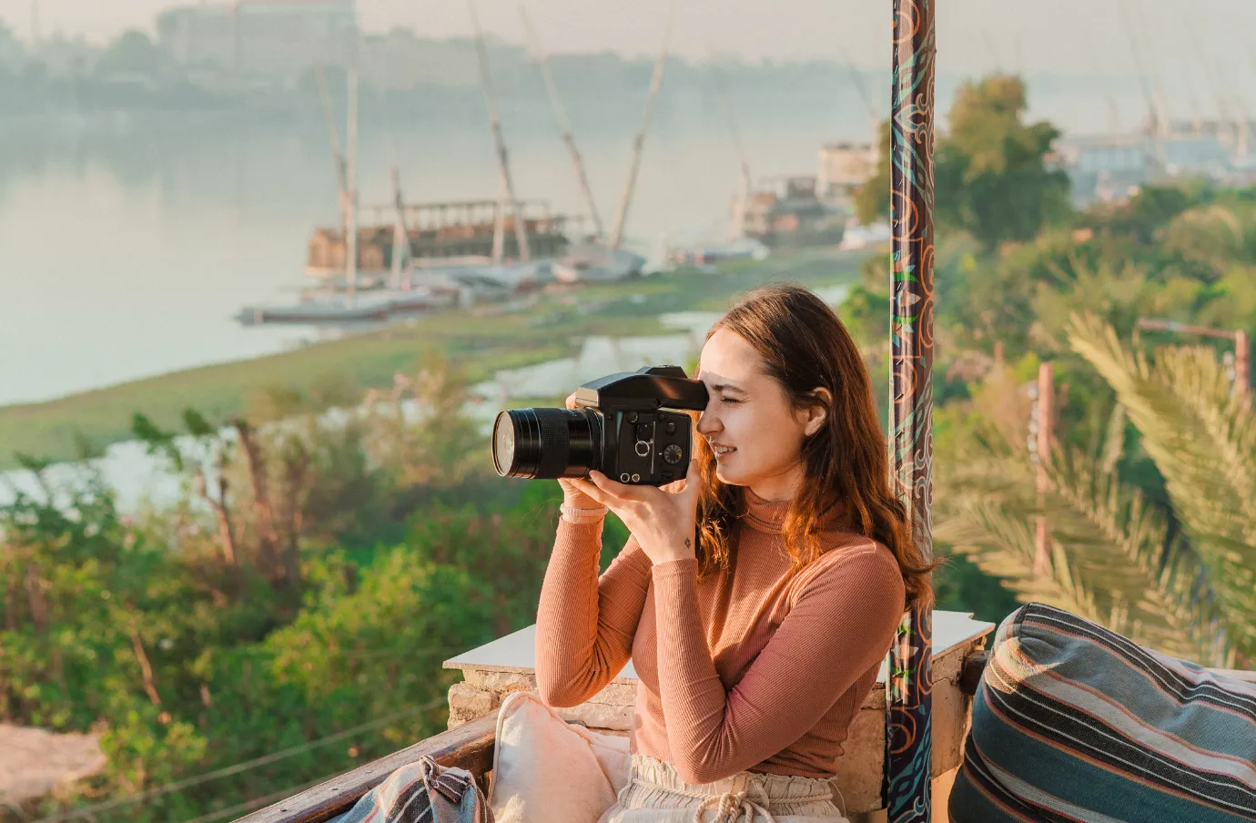 a woman with brown hair and travel insurance for Egypt holds a camera up to her face to take pictures of the Nile River