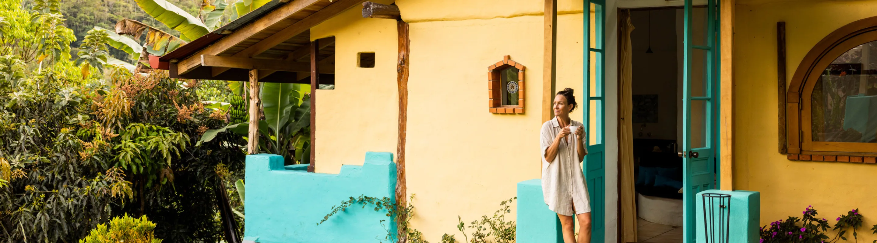 a woman with travel insurance for Costa Rica stands outside her accommodations and drinks coffee on the front porch