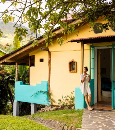 a woman with travel insurance for Costa Rica stands outside her accommodations and drinks coffee on the front porch