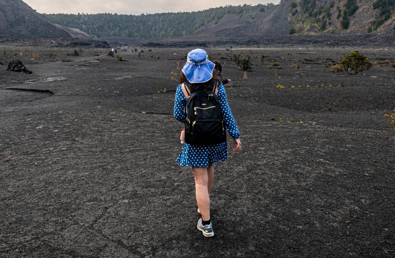 a woman in blue hikes a volcanic landscape, insured with volcano travel insurance 