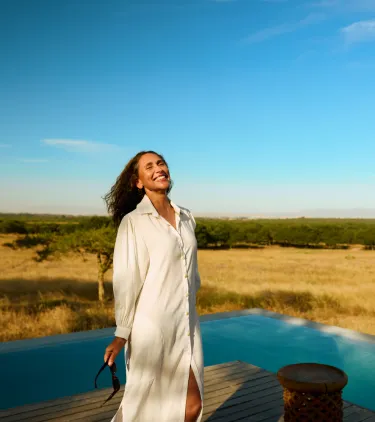 a woman stands in front of an infinity pool at a luxury safari lodge, insured with travel insurance for Africa 