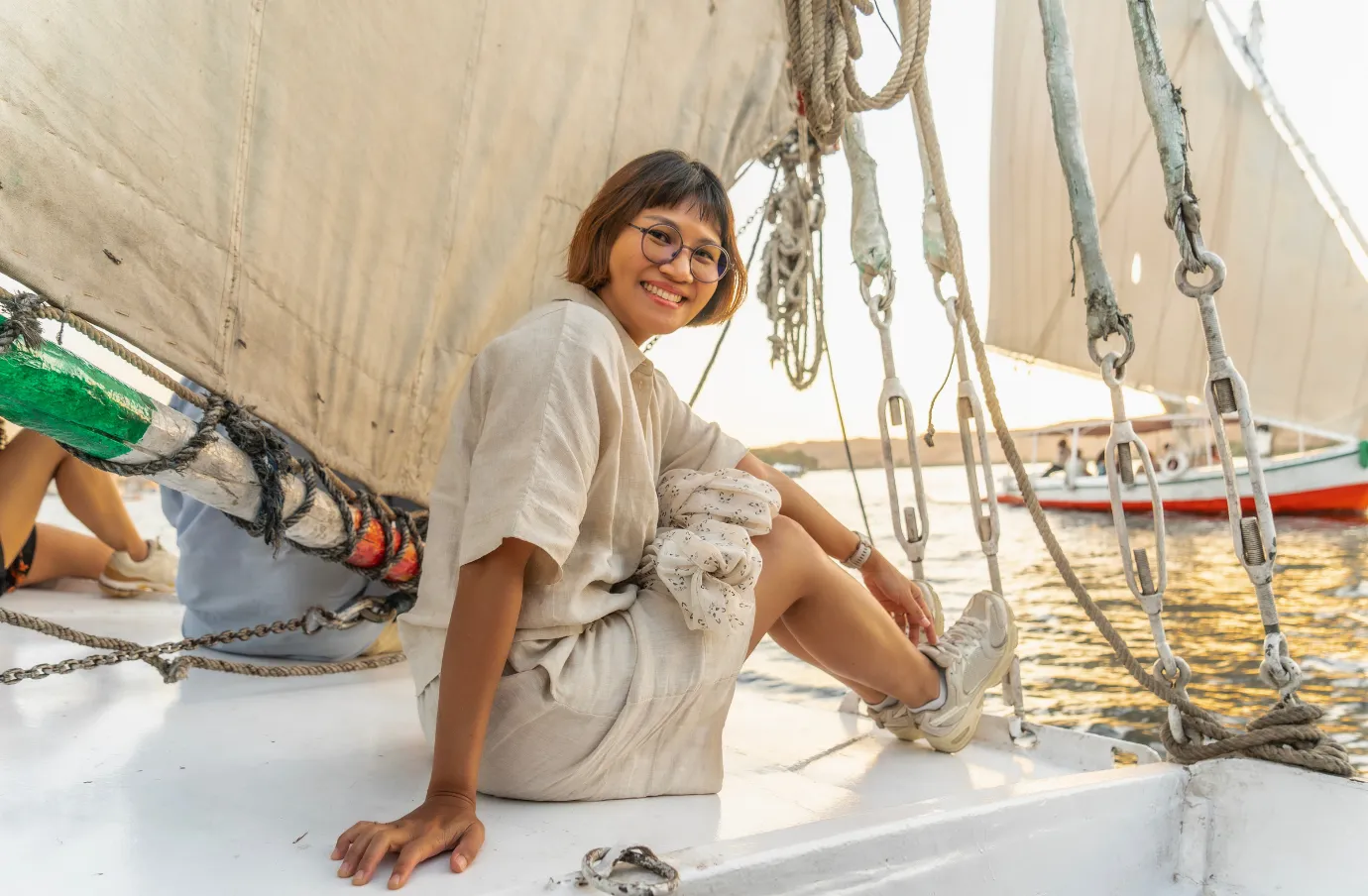 a woman smiles and she sails the Nile River on an Egyptian felucca boat, insured with travel insurance for Egypt