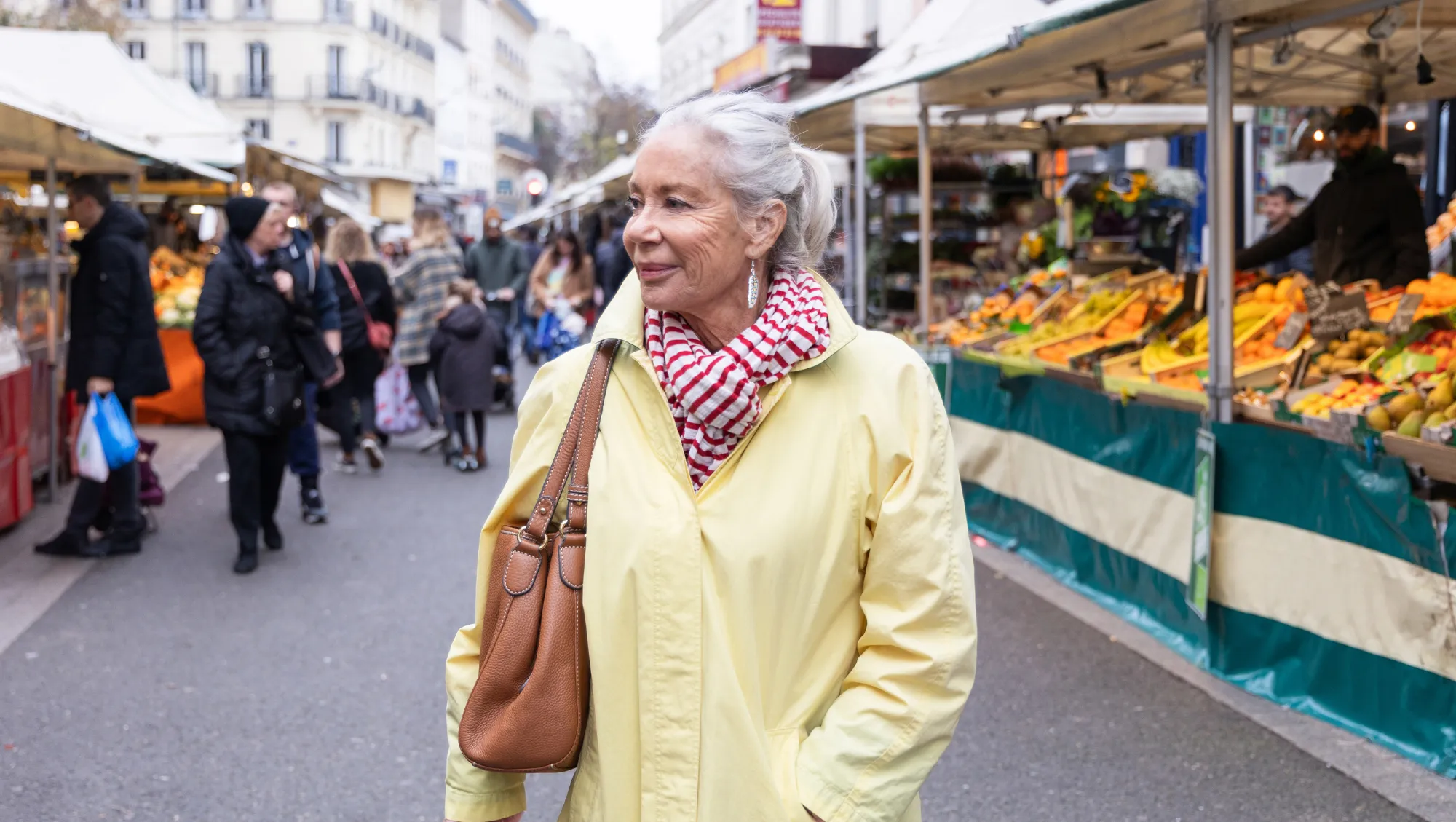 a woman in a yellow coat shops at a market in Paris, holding her purse close to prevent theft on vacation