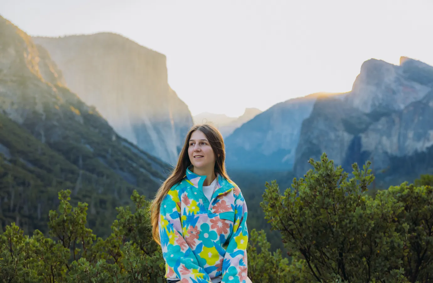 a woman in a flower sweater stands in Yosemite Valley at sunrise, insured with travel insurance for California 