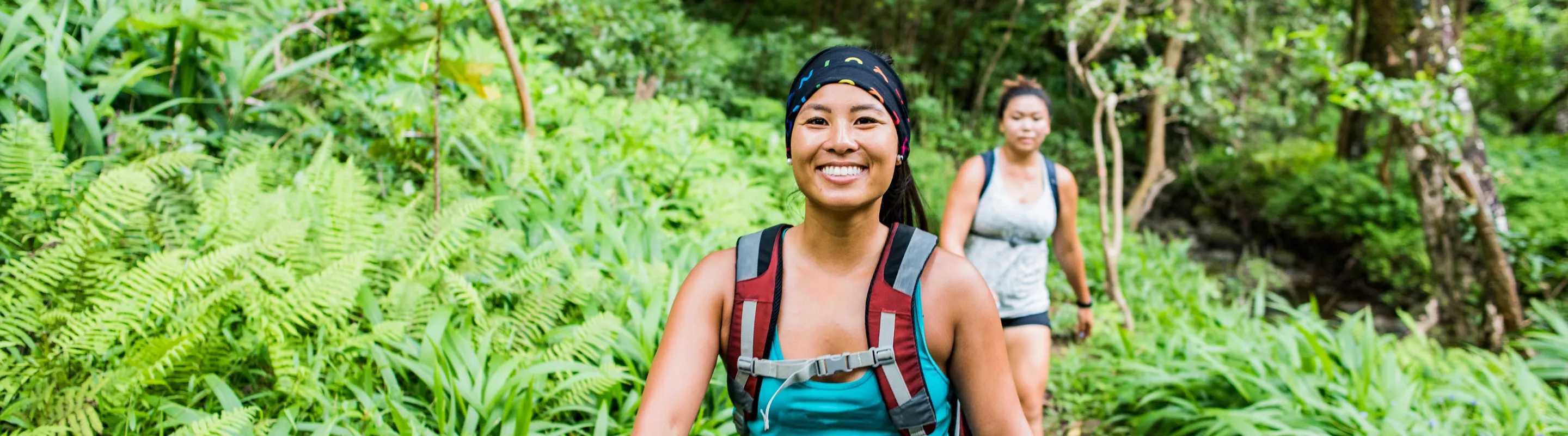 two young women hike a tropical trail, insured with travel insurance for Hawaii