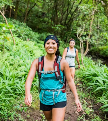 two young women hike a tropical trail, insured with travel insurance for Hawaii