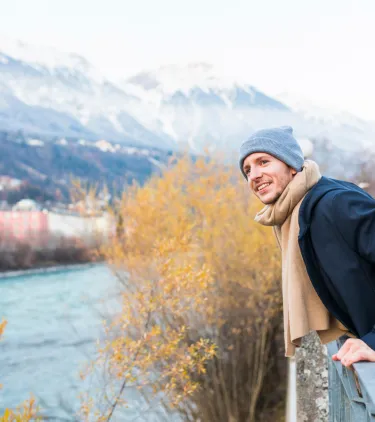 a young man with travel insurance for Austria overlooks the scenic town of Innsbruck in winter clothes 