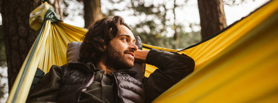 Smiling man looking away while lying over hammock in forest, a top camping site according to the United States travel guide he read