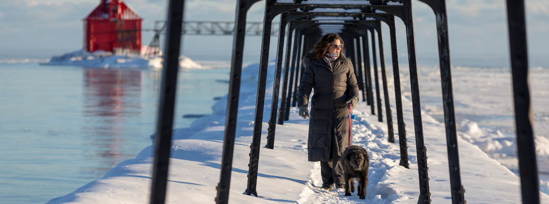Woman walking her dog in snow lined by icy water in wisconsin, one of the best places to travel as a solo female U.S.