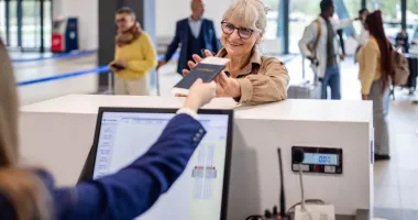 Senior woman smiling and receiving her passport at airport counter may wonder, "Do I need a REAL ID to fly?"