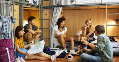 Five young adults laughing and talking in a hostel after researching are hostels safe