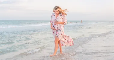 woman holding her belly while walking on the beach and traveling during pregnancy