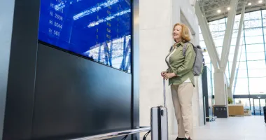 senior woman smiling at the flight monitor in the airport and wondering if travel insurance covers flight disruptions