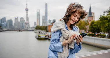 Young woman using our travel app on her smartphone with Shanghai in the background