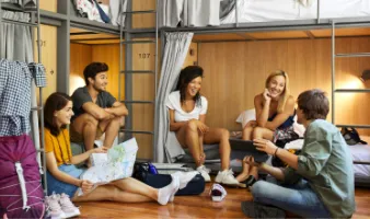 Five young adults laughing and talking in a hostel after researching are hostels safe