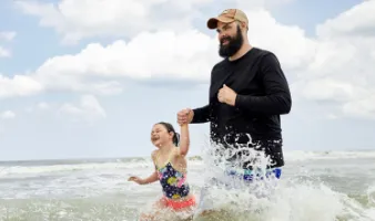 father holding daughter's hand and walking through waves in the Florida ocean during hurricane season