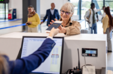 Senior woman smiling and receiving her passport at airport counter may wonder, "Do I need a REAL ID to fly?"