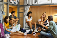 Five young adults laughing and talking in a hostel after researching are hostels safe
