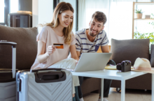Young couple with laptop and suitcases choosing between credit card travel insurane and a policy.