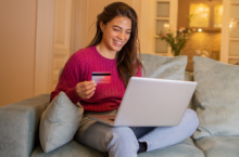 Young woman holding a credit card and using her laptop to look up how much is travel insurance