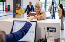 Senior woman smiling and receiving her passport at airport counter may wonder, "Do I need a REAL ID to fly?"