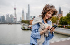 Young woman using our travel app on her smartphone with Shanghai in the background