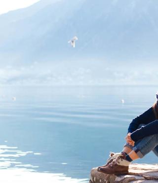 Young woman relaxing at winter sea beach. Traveler resting by blue mountain